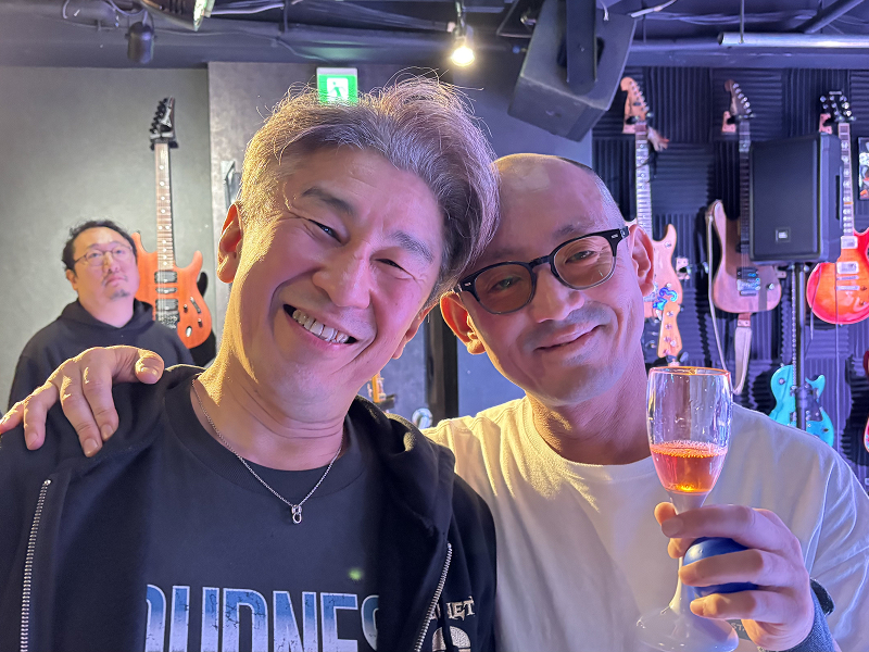 笑顔でグラスを掲げて肩を組む男性2人